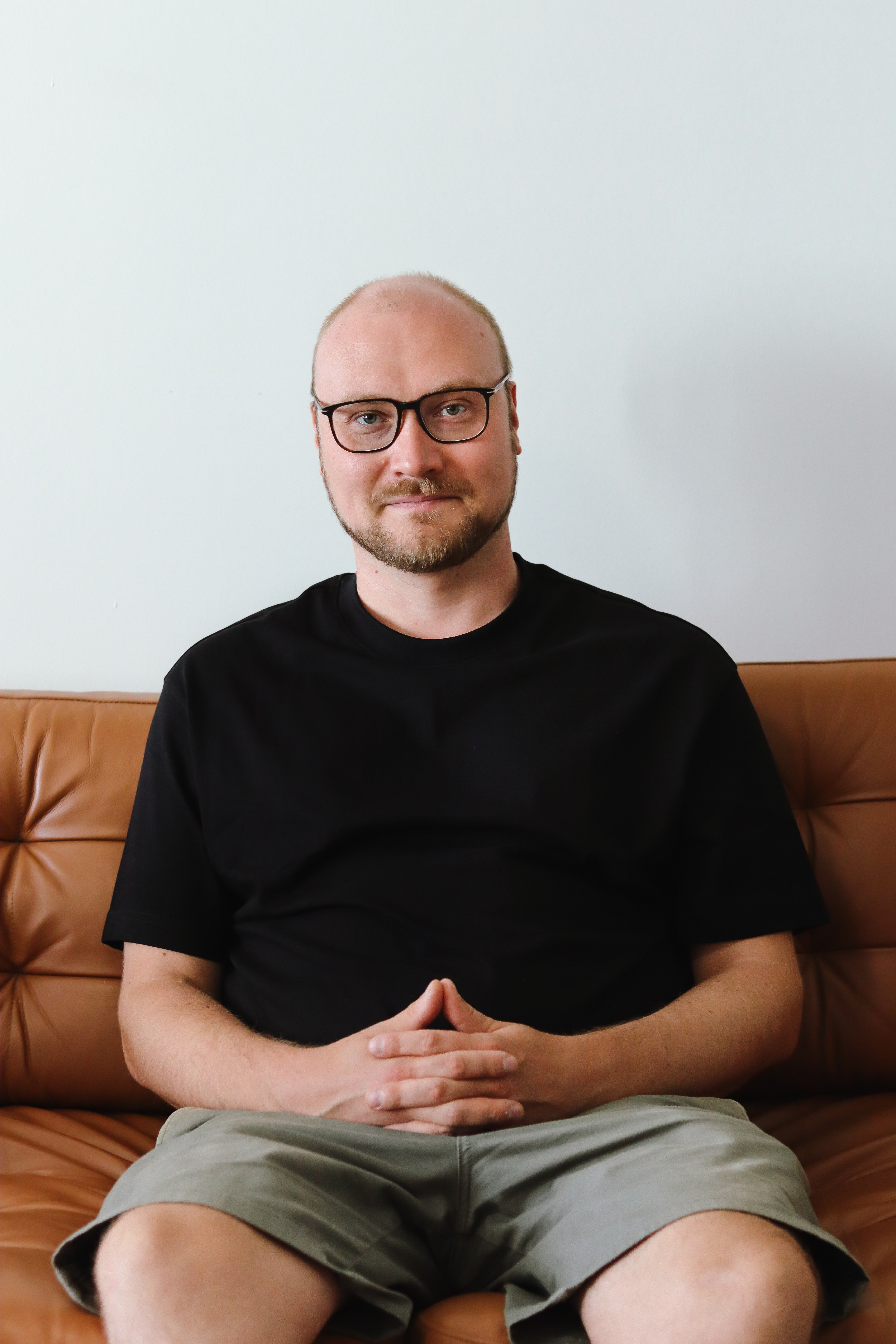 Komea mies istuu sohvalla kädet ristissä ja hymyilee kameralle